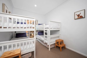 A room with bunk beds, a small wooden stool, and a framed picture on the wall. - Beach Comber (Anglesea)