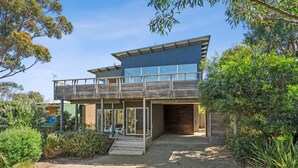 A modern two-story house with a balcony, a covered porch, and a driveway leading to the entrance. - Beach Comber (Anglesea)