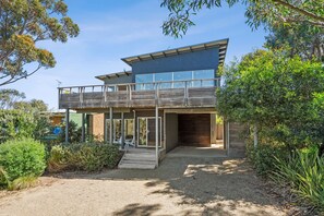 A modern two-story house with a balcony, a covered porch, and a driveway leading to the entrance. - Beach Comber (Anglesea)