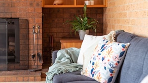 Ein gemütliches Wohnzimmer mit Kamin, einer Couch mit floralen Kissen und einer Zimmerpflanze.