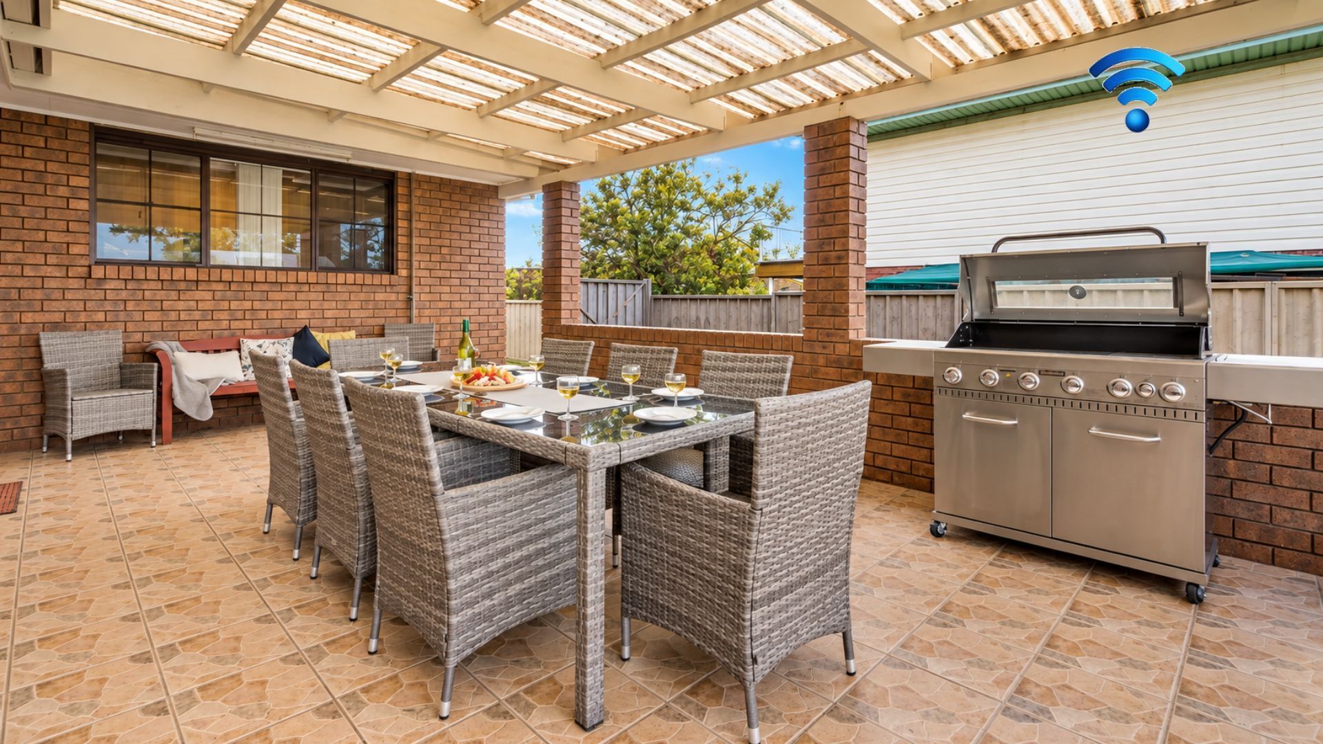 An outdoor patio with a brick wall, a grill, wicker furniture, and a tiled floor.