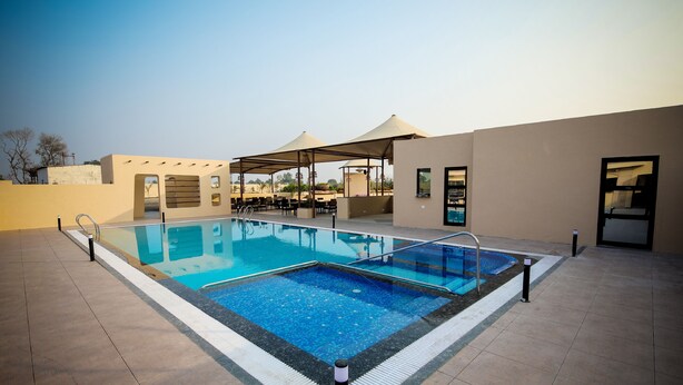 A swimming pool with a tiled deck, outdoor seating, and covered areas. - Enrise by Sayaji Rewa (Huzur)