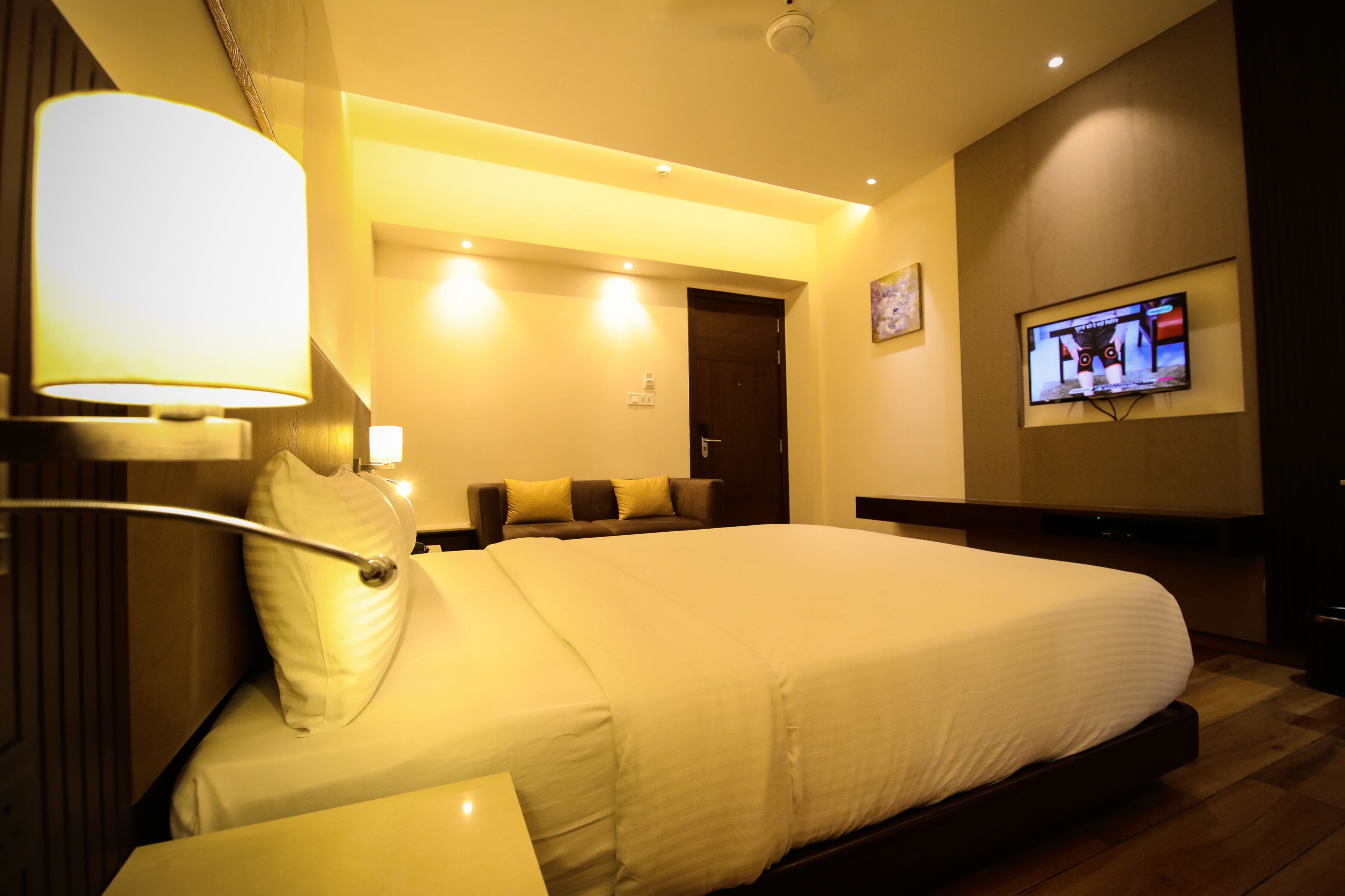 Une chambre d’hôtel avec un grand lit, un téléviseur à écran plat fixé au mur et une lampe moderne.