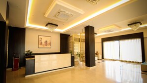 A hotel reception area with a reception desk, a large window with curtains, and a chandelier. - Enrise by Sayaji Rewa (Huzur)