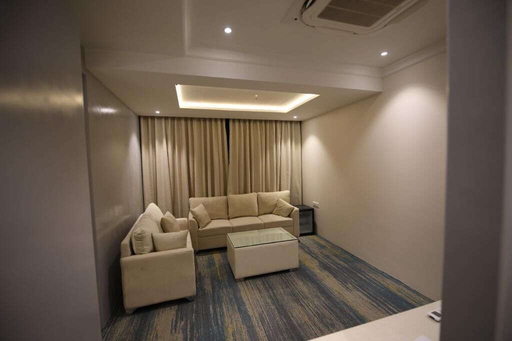 Une chambre d’hôtel moderne, dotée d’un canapé d’angle, d’un fauteuil plus petit, d’une table basse en verre et d’un téléviseur à écran plat.
