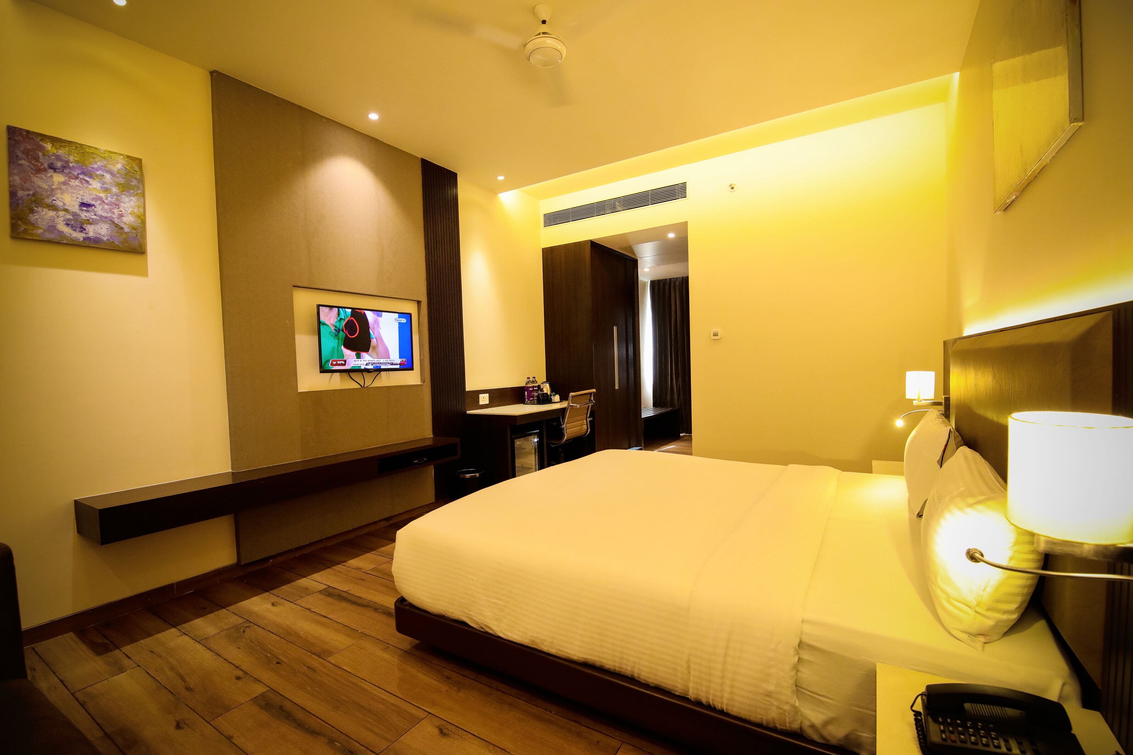 A hotel room with a bed, bedside lamp, TV, desk, and a mirror.