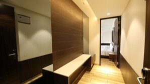 A modern hotel hallway with a wooden bench, a mirror, and a door leading to a room with a bed. - Enrise by Sayaji Rewa (Huzur)