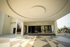 Una entrada de edificio con suelo de baldosas geométricas, diseño de techo circular y puertas de cristal.