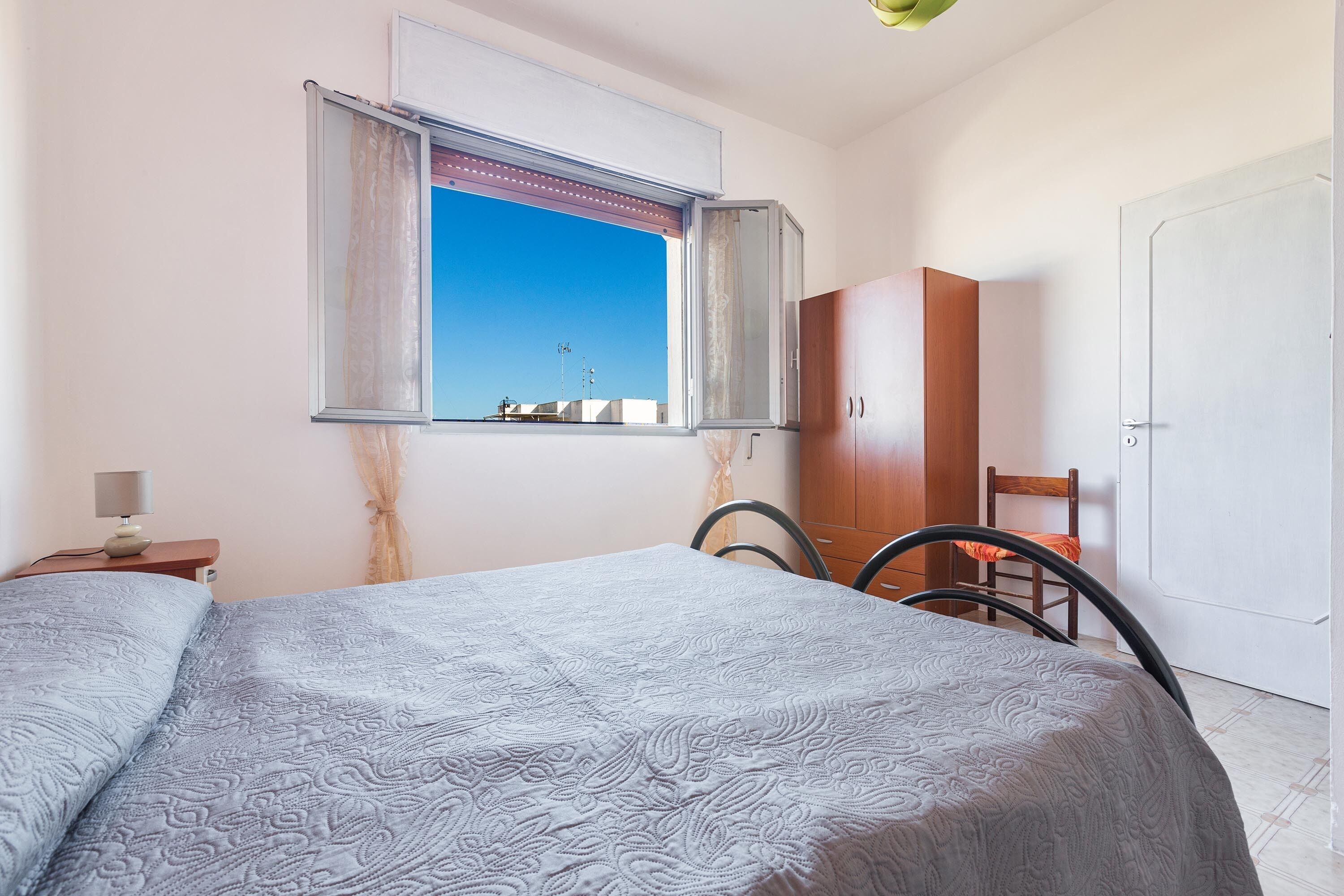 A bedroom with a bed, a window with curtains, a wardrobe, and a chair.