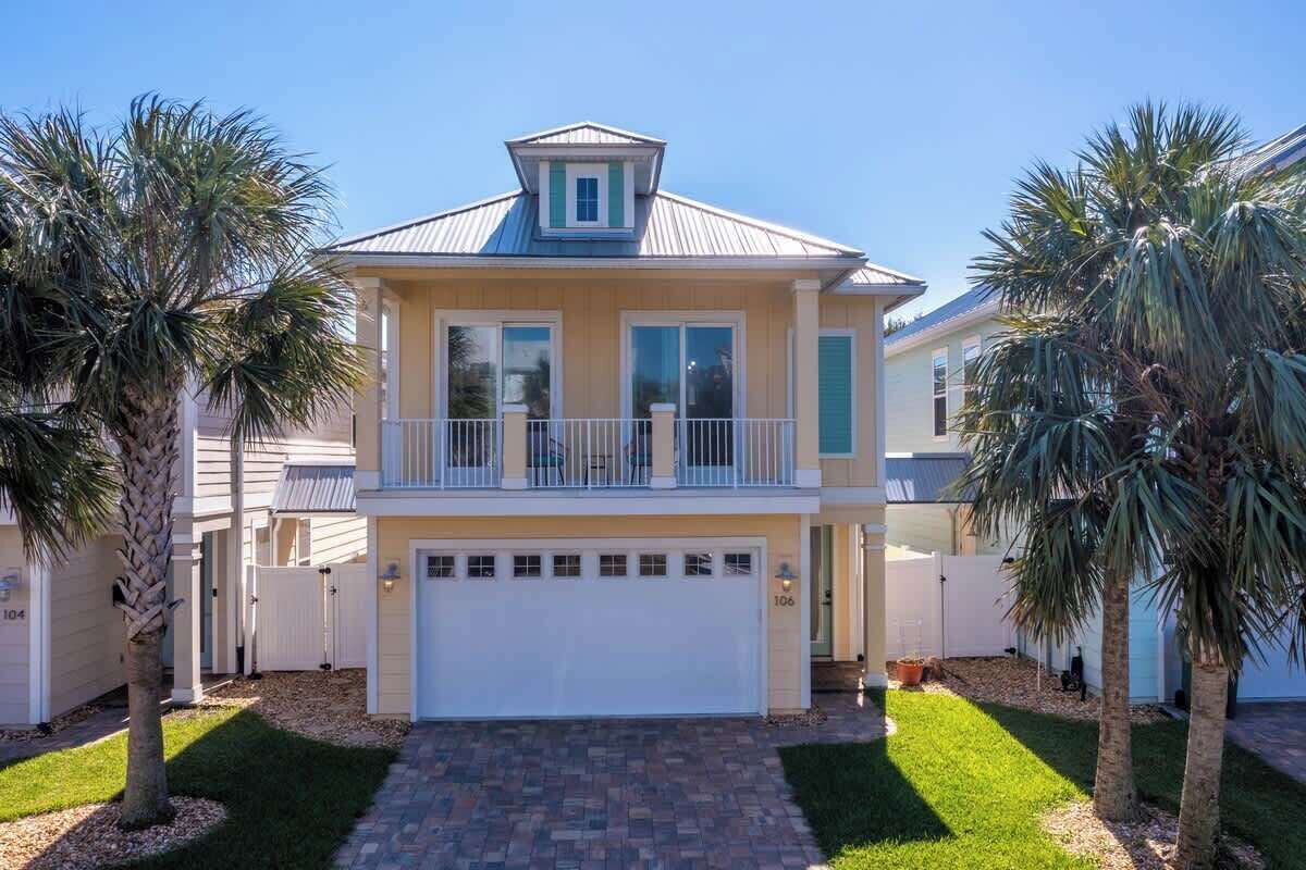 A two-story house with a garage, a balcony, and palm trees in the yard.