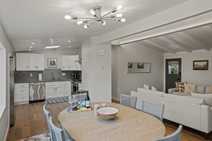 Een moderne keuken met witte kastjes, een eethoek met een ronde tafel, en een woonkamer met een bank.