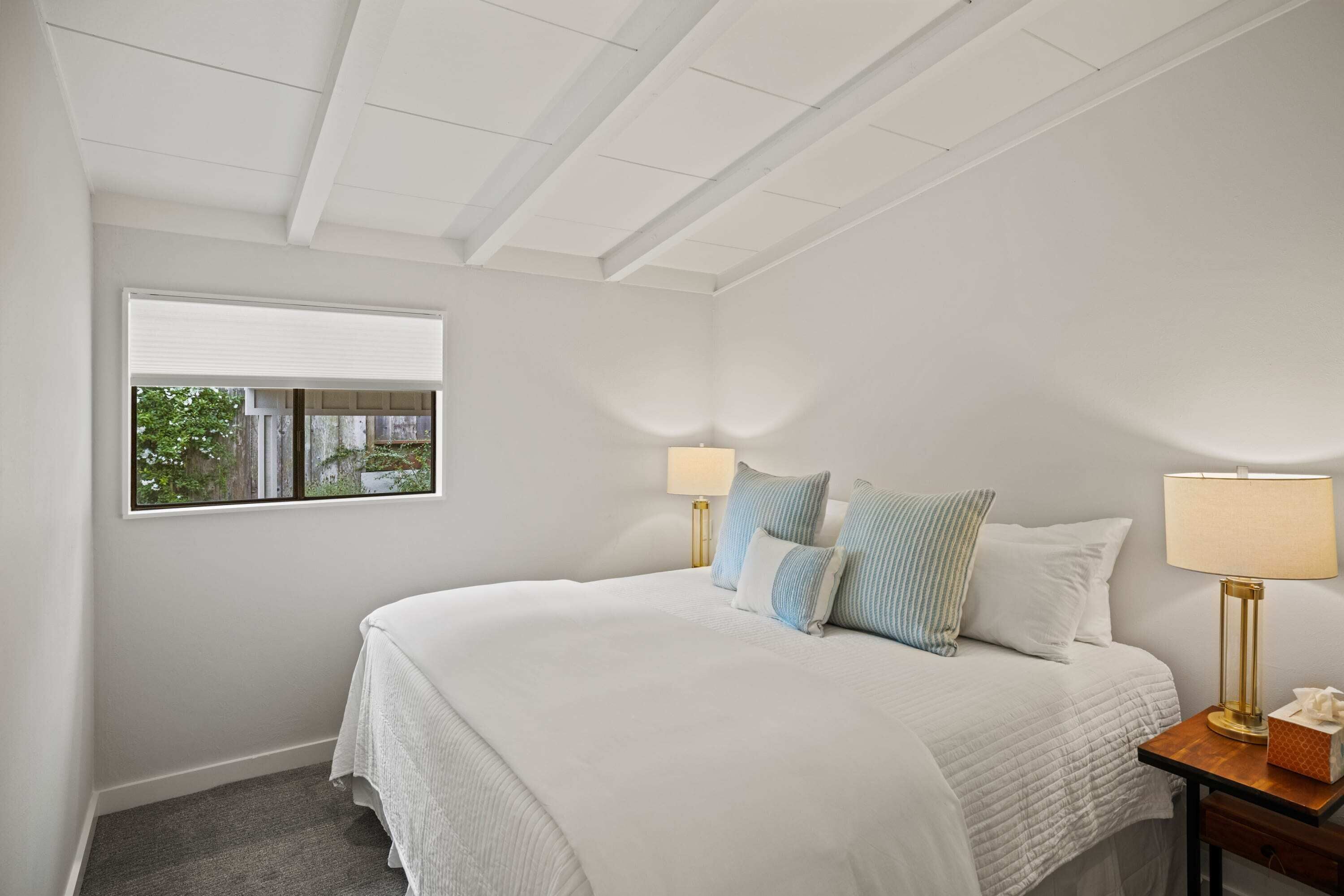 A bedroom with a bed, two bedside lamps, a window with blinds, and a nightstand.