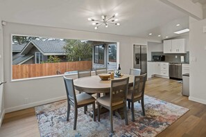 Een moderne keuken met witte kastjes, roestvrijstalen apparatuur en een eethoek met een ronde tafel en stoelen.