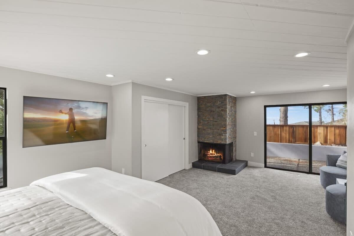Un dormitorio con cama, chimenea, un ventanal grande y un cuadro.