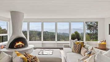 Una sala de estar moderna con chimenea, ventanas grandes y vistas al exterior.