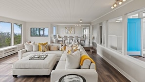 Een moderne woonkamer met een modulaire bank, een eethoek en grote ramen met uitzicht.