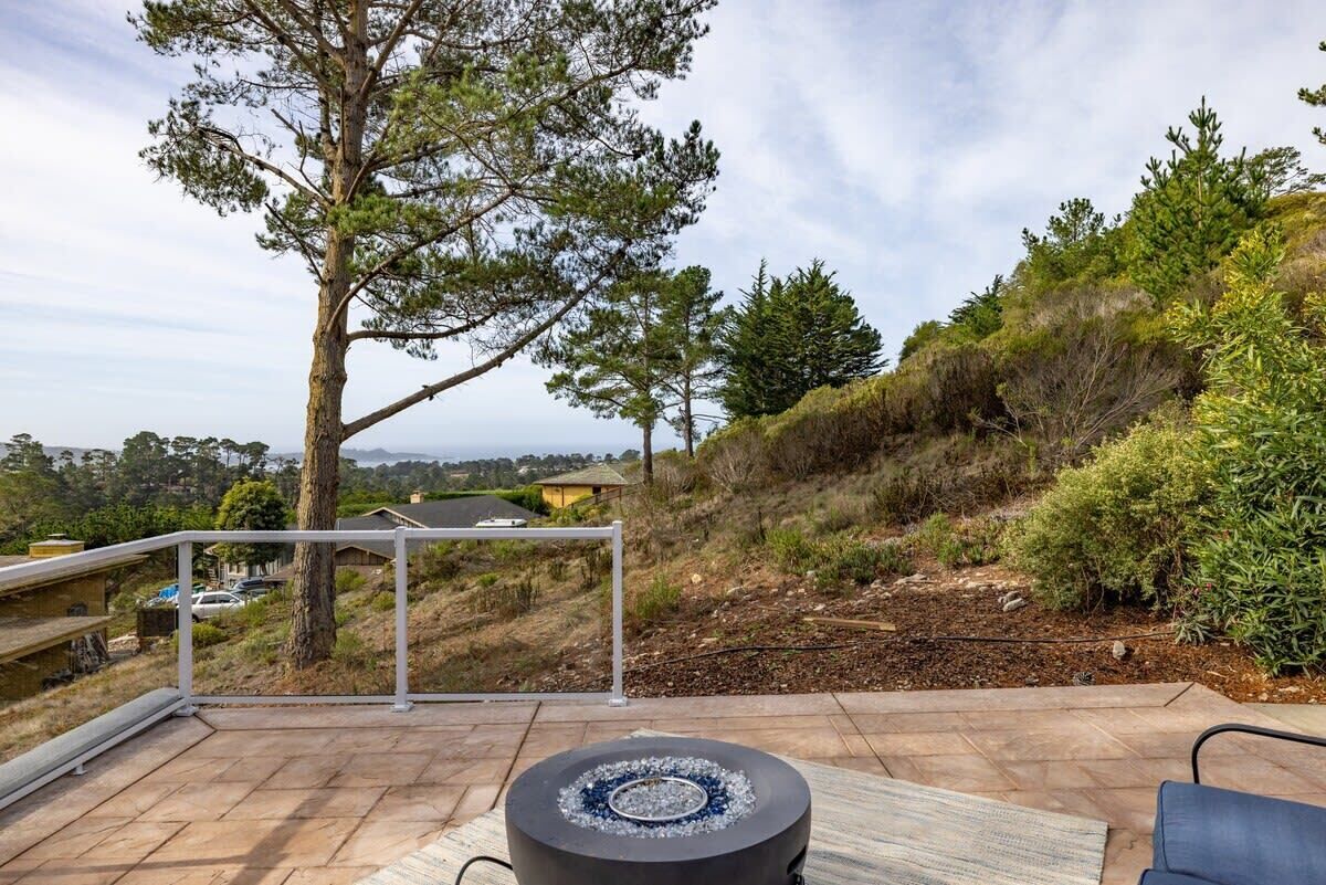 Un patio con un pozo de fuego, mobiliario exterior y vistas a una colina con árboles y un edificio distante.