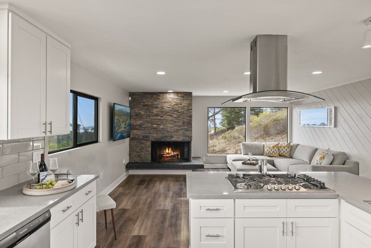 Una cocina moderna con chimenea de piedra, armarios blancos y un comedor con sofá gris.