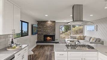 Una cocina moderna con chimenea de piedra, armarios blancos y un comedor con sofá gris.