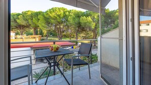 Varanda com mesa e cadeiras, uma tigela de frutas e vista para árvores e edifícios.