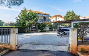 Un camí d'accés amb porta tancada que condueix a una casa de dos pisos, amb un cotxe estacionat al camí.