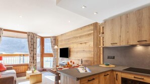 A modern kitchen with wooden cabinetry, a built-in oven, and a large window overlooking a balcony. - Le Borsat (Val Claret) by Interhome (Tignes)
