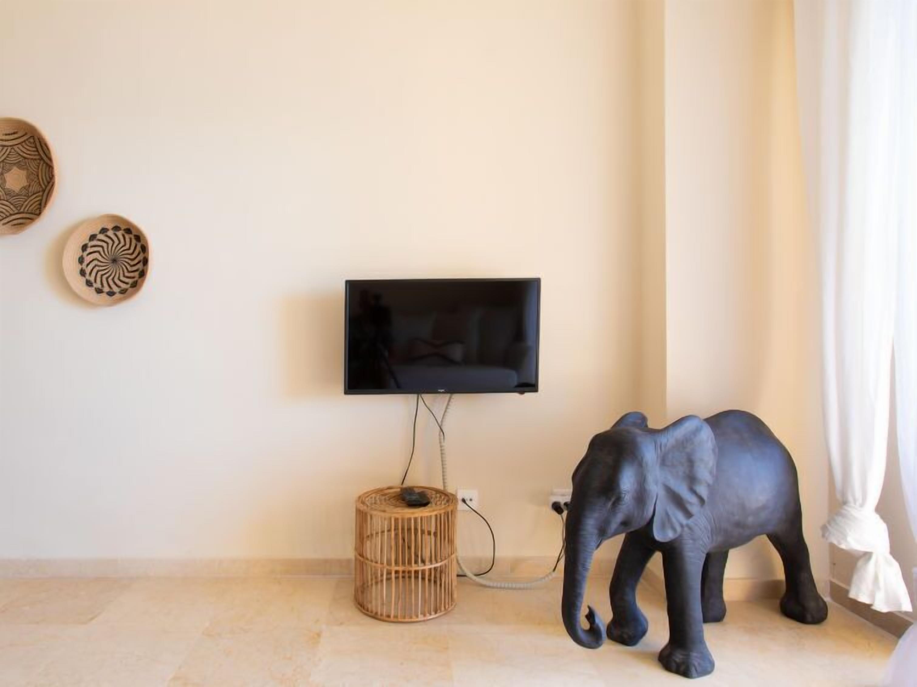 A room with a mounted TV, a wicker basket, and a statue of an elephant.