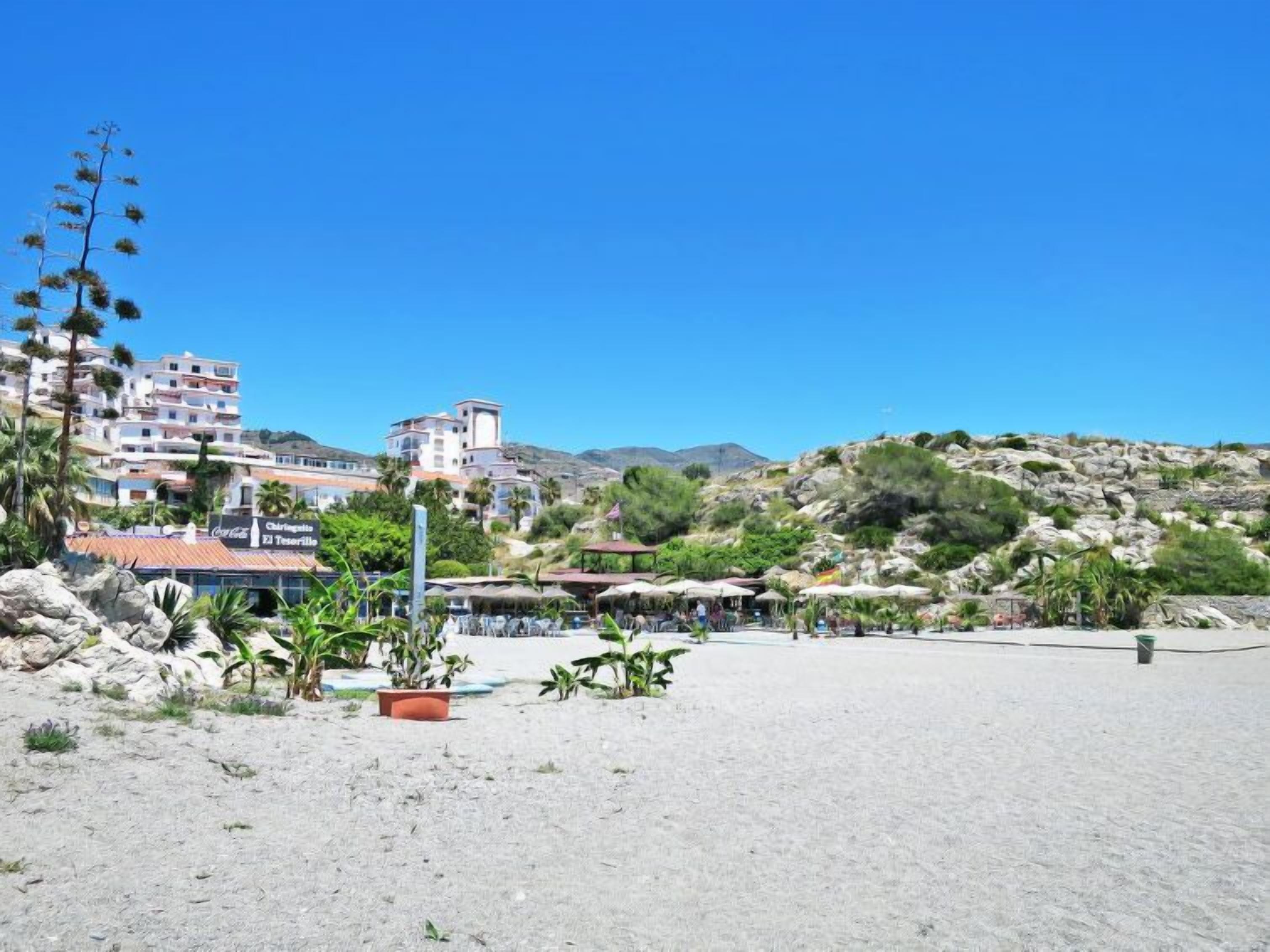 Una zona costiera con edifici, una spiaggia sabbiosa e un terreno roccioso.