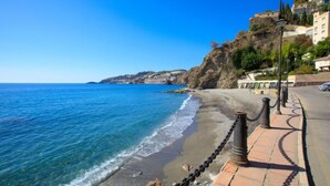 A coastal walkway with a clear view of the sea, a rocky cliff, and buildings in the background. - Sea Suite by Interhome (Almuñécar)