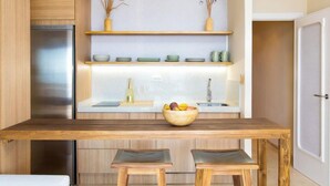 A modern kitchen with wooden cabinets, a stainless steel refrigerator, a wooden dining table with two stools, and a fruit bowl on the counter. - Sea Suite by Interhome (Almuñécar)