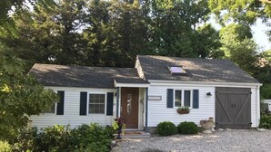 A white cottage with a front door, a garage, and a small porch with a potted plant.