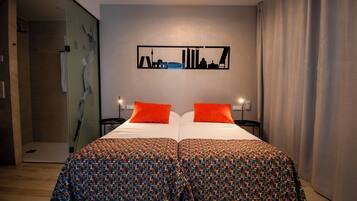 Una cama doble con dos almohadas naranjas, una colcha estampada y una obra de arte con motivo de paisaje urbano en la pared.