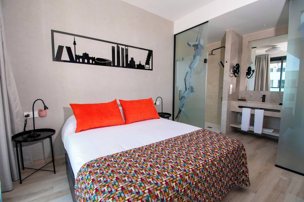 Habitació d'hotel amb llit, una obra d'art amb paisatge urbà, bany amb dutxa i mirall.