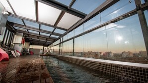 A glass-enclosed indoor pool with a city view, metal railings, and a tiled floor. - E-kilibrio Hotel & Apart-Suites (Madrid)