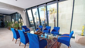 A conference room with a glass table surrounded by blue chairs, large windows, and a view of palm trees. - E-kilibrio Hotel & Apart-Suites (Madrid)