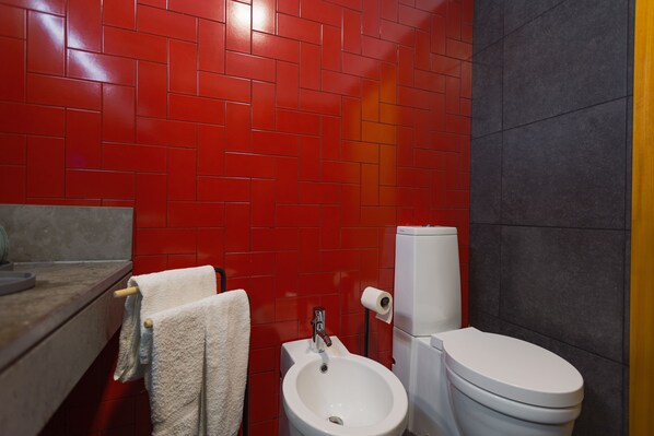 A bathroom with red tiled walls, a white sink, and a toilet. - Secret Beach House (Água de Alto)