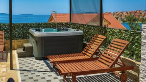 Un balcon doté d’un jacuzzi, de deux fauteuils de relaxation en bois et offrant une vue sur la mer et les bâtiments.