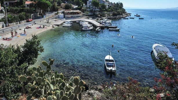 Une ville côtière dotée d’un port abrité, où des bateaux sont amarrés, et d’une plage animée.