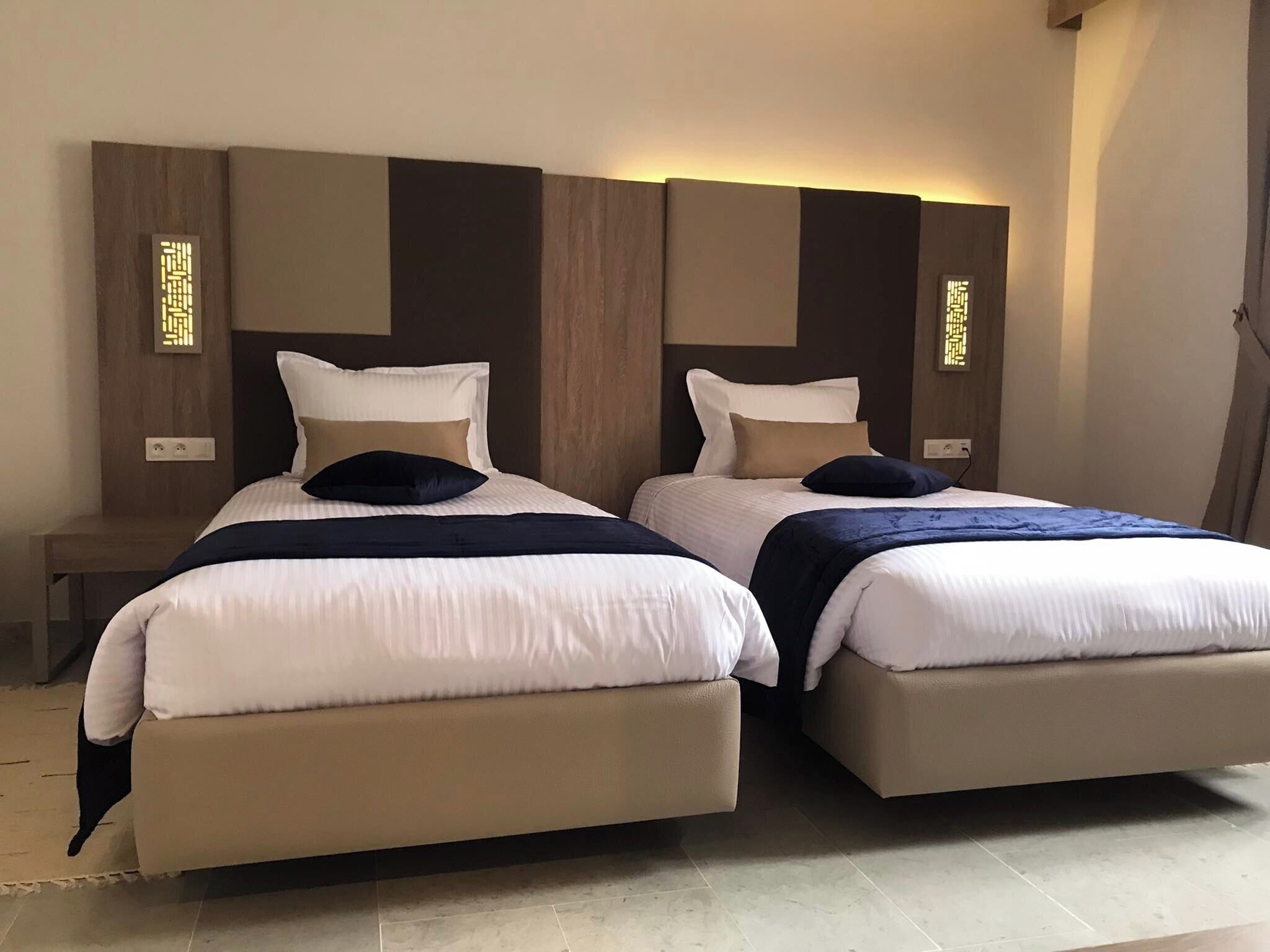 A hotel room with two beds, a nightstand, and a wall-mounted light fixture.