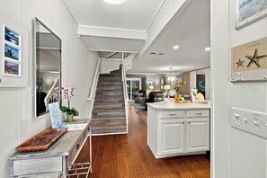 Polished wood floors lead your eye through this airy entryway, where crisp white shiplap and marble counters glow under soft lighting. A weathered console and nautical accents create a coastal charm that feels instantly like home.
