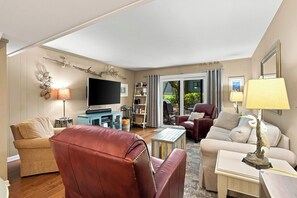 A living room with a flat-screen TV, leather sofas, a coffee table, and a bookshelf. - Beachside Luxury Villa w/ Pool on Hilton Head (Hilton Head Island)