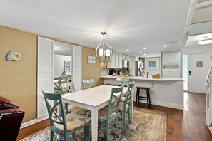 A modern kitchen with white cabinets, a central island, and a dining area with a white table and teal chairs.