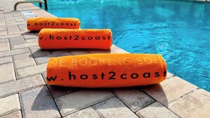 Drie oranje handdoeken met 'www.host2coast' erop, neergelegd bij een zwembad.