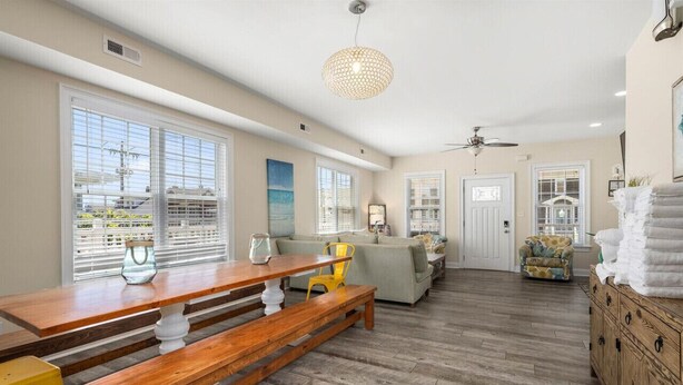A spacious living area with a wooden dining table, benches, a sofa, and a patterned armchair.