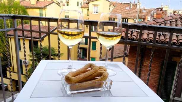 Un balcon avec une table, deux verres de vin blanc et un plat en verre contenant des bretzels.