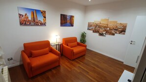 Une pièce avec deux fauteuils orange, une petite table avec une lampe et un grand tableau représentant un paysage urbain accroché au mur.