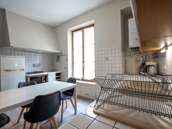 A kitchen with a dining table, chairs, a refrigerator, a stove, and a window.