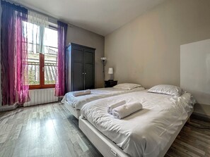 A bedroom with two beds, a wardrobe, a bedside lamp, and a window with curtains.