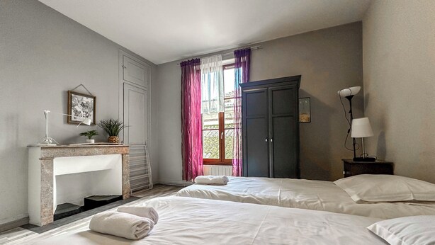 A hotel room with two beds, a desk with a lamp, a fireplace, and a view of the outdoors.