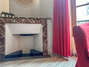 A room with a fireplace, a red curtain, and a wooden floor.